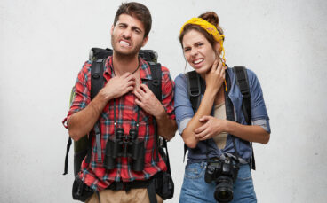 Portrait of angry young couple scratching, feeling annoyed while being bitten by exotic insects or Mosquitos, looking at camera with painful expression on their faces. Tourism, travel and adventure
