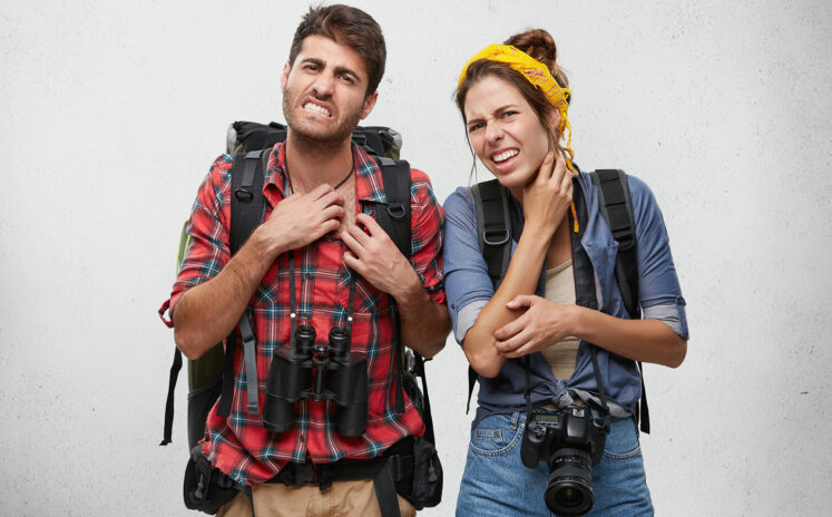 Portrait of angry young couple scratching, feeling annoyed while being bitten by exotic insects or Mosquitos, looking at camera with painful expression on their faces. Tourism, travel and adventure
